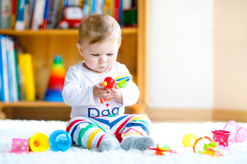 Adorable baby girl playing with educational toys in nursery. Happy healthy child having fun with colorful different toys at home. Baby development and first steps, learning to play and to grab.