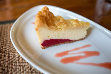 A piece of strawberry cheese cake with strawberry sauce on white plate.