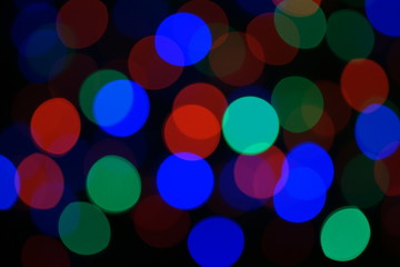Multi-color blue holiday garland. Garland is blurred. Many big colorful round lights. Fully defocused photo. Blurred background and foreground. Holiday mood. New Year and Christmas is coming.
