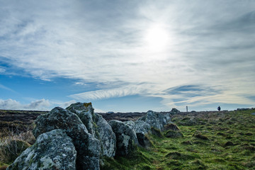 meadow landscape in spring; gray boulders line from close up go far, right side is green meadow with human silhouette in the distance, beautiful, cloudy sky