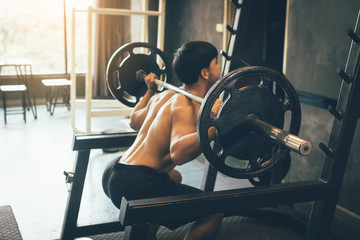 Fototapeta na wymiar Asian man performing barbell squats at the indoor gym.