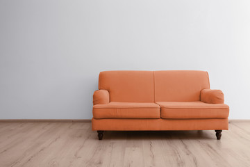 Orange sofa in room near white wall. Space for text