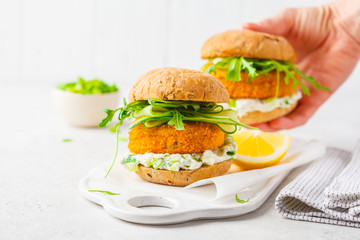 Fish burger with cucumber, arugula and mayonnaise sauce, white background, copy space.