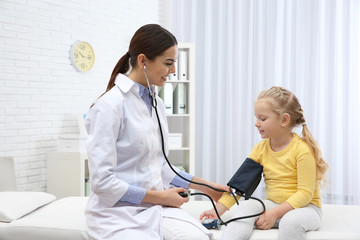 Little girl visiting doctor in hospital. Measuring blood pressure and checking pulse