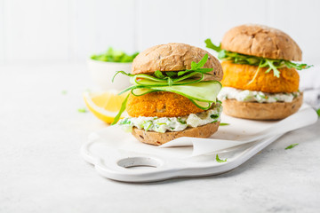 Fish burger with cucumber, arugula and mayonnaise sauce, white background, copy space.