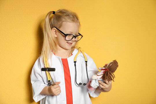 Cute Child Imagining Herself As Doctor While Playing With Reflex Hammer And Doll On Color Background