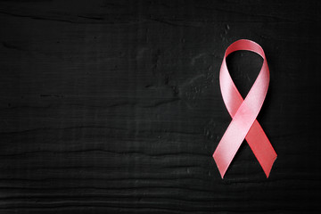 Pink ribbon on wooden background, top view with space for text. Breast cancer concept