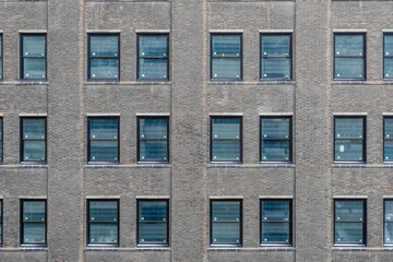 Side of brick skyscraper in dense urban area with blue windows