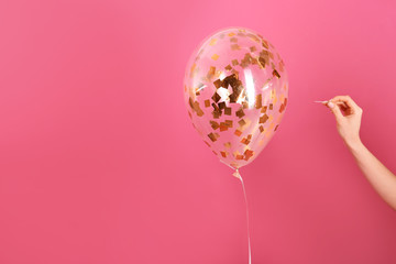 Woman piercing balloon with needle on color background, closeup. Space for text