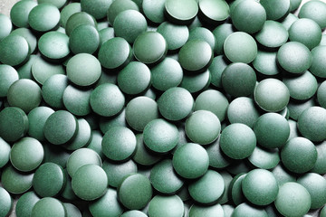 Green spirulina pills as background, closeup view