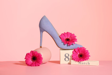 Composition with high heeled shoe and flowers on table against color background. International Women's Day
