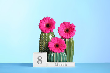 Composition with decorative cacti and flowers on table against color background. International Women's Day