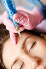 Professional beautician doing eyebrow tattoo at woman face. Permanent brow makeup in beauty salon,...