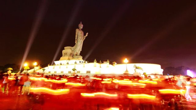 People walks with lighted candles in hand around buddha image