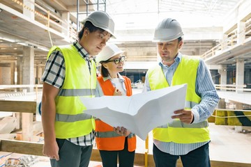 Group of engineers, builders, architects on the building site, looking in blueprint. Construction,...