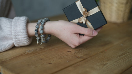 girl holds a gift box tied with a ribbon, on her arm are two tourmaline bracelets, a bracelet made...