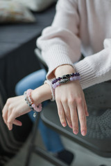 hands on the back of a chair, four bracelets of purple, pink, gray, stones on the hand, bracelets of amethyst, rose quartz, tourmaline quartz, sherl, charoite (vertically, close up)