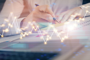 Close up of hands writing with double exposure of business charts. Financial concept.