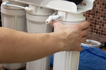 plumber change the water filter. installing osmosis in home. male hand spins the cartridge