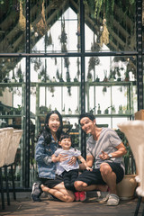 Cute little girl and her beautiful young parents looking at camera and smiling . Smiling young parents and their child are very happy, they are at cafe.