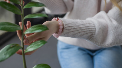 the girl has rose quartz bracelets, the girl is holding a branch with green leaves, the girl is holding a indoor flower (horizontally).
