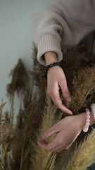 a girl with bracelets of pink quartz and amethyst hands on a bouquet of dry grass