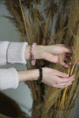 a girl with rose quartz and amethyst bracelets holds a bouquet of dry grass, the girl has bracelets on her hands