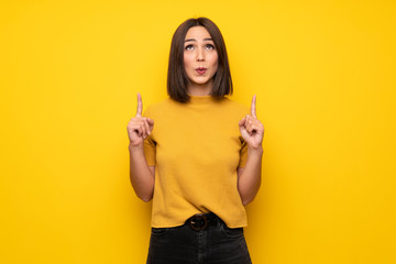 Young woman over yellow wall pointing up and surprised