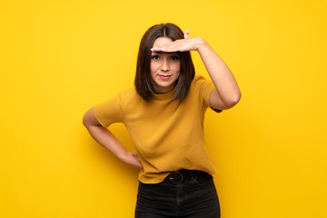 Young woman over yellow wall looking far away with hand to look something