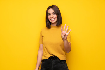 Young woman over yellow wall happy and counting four with fingers