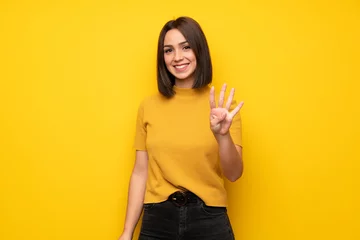Fotobehang Young woman over yellow wall happy and counting four with fingers © luismolinero