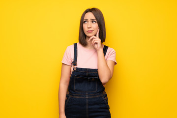 Young woman over yellow wall thinking