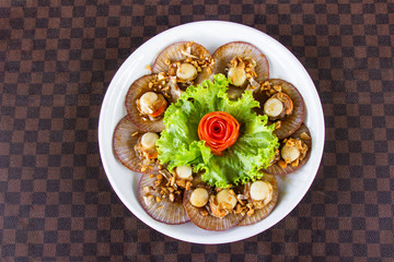 Fried scallops with garlic decorated with carrots on a white ceramic dish put on leather floor the grid pattern. Top view