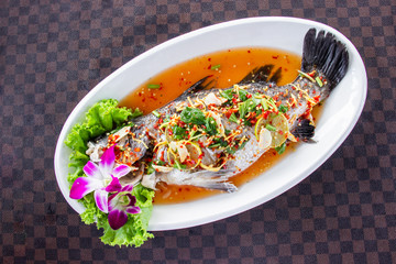 Steamed sea bass fish with lemon put a white ceramic dish on leather floor the grid pattern. Top view.
