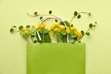 Yellow primrose flowers in a green shopping bag with space for text on yellow paper