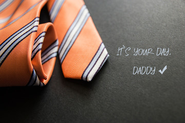 Close - up photo orange men's tie. Text for holiday card or banner on black background