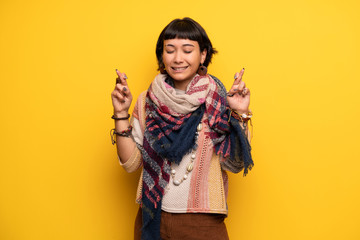 Young hippie woman over yellow wall with fingers crossing and wishing the best