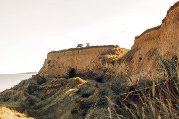 Fototapeta premium Beautiful view of sandy cliff near sea beach. Landscape of beach cliff with green grass. Summer vacation concept. Exploring interesting places