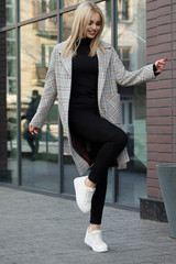 Beautiful young stylish blonde woman wearing coat walking through the city streets. Trendy casual outfit. Street fashion.