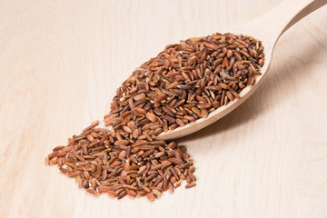 Brown rice in a wooden spoon on a wooden board.