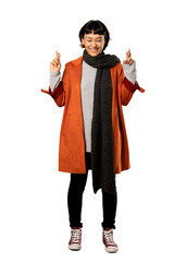 A full-length shot of a Short hair woman with coat with fingers crossing and wishing the best over isolated white background