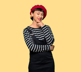 Young woman with beret thinking an idea while looking up over yellow background