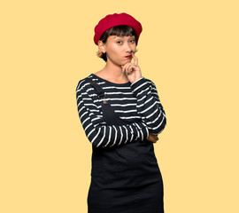 Young woman with beret thinking over yellow background