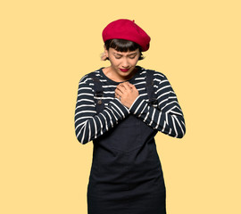 Young woman with beret having a pain in the heart over yellow background