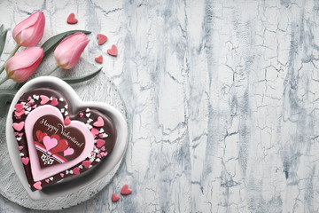Valentine heart cake with chocolate,decorations and text "Happy Valeitine" and a bunch of pink tulips, copy-space