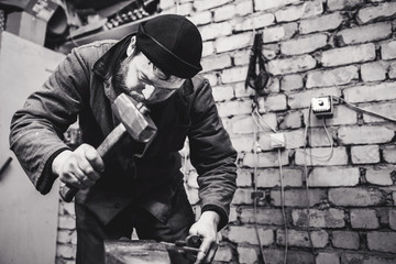 The blacksmith manually forging the red-hot metal on the anvil.