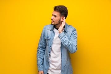 Fototapeta premium Handsome man over yellow wall listening to something by putting hand on the ear