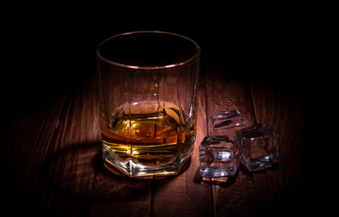 A glass of whisky and some ice cubes on the wooden table