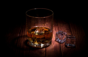 A glass of whisky and some ice cubes on the wooden table