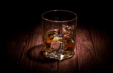 A glass of whisky and some ice cubes on the wooden table